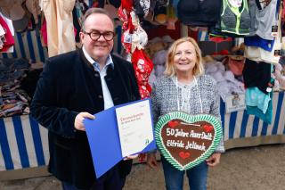 Auf der Kirchweihdult 2024 ehrte der Referent für Arbeit und Wirtschaft Clemens Baumgärtner die Beschickerin Elfriede Jelinek für ihr langjähriges Engagement auf der Auer Dult. Auf der Kirchweihdult 2024 ehrte der Referent für Arbeit und Wirtschaft Clemens Baumgärtner die Beschickerin Elfriede Jelinek für ihr langjähriges Engagement auf der Auer Dult.